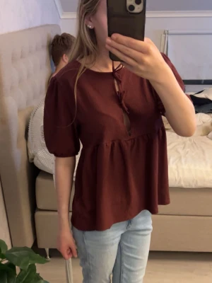 Vinröd blus med puffärm och knyt - Söt vinröd blus med puffärmar och knyt framtill.Blusen är knappt använd så i fint skick.