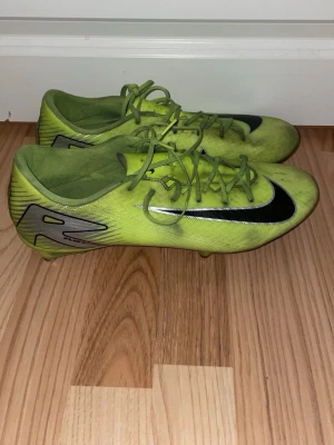 Nike Mercurial - Säljer ett par gula Nike fotbollsskor med svart swoosh och silverdetaljer på hälen. Skorna har klassisk låg profil och snörning för bra passform. Perfekta för dig som vill sticka ut på planen och få grym kontroll på bollen. Använda men inga hål, storlek 45