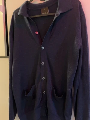 Mörkblå cardigan från Oscar jacobsson - Mörkblå cardigan med knappar framtill och två fickor. Långärmad med klassisk krage och mjukt, tunt material. Perfekt att slänga över en t-shirt eller skjorta för en chill look. Den är storlek L men sitter mer som M