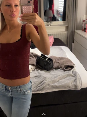 Vinröd glittrig linnetopp - Snygg vinröd linnetopp med glittriga detaljer och breda axelband. Toppen är croppad och har en fyrkantig ringning. Perfekt att styla med jeans eller kjol för en trendig look.