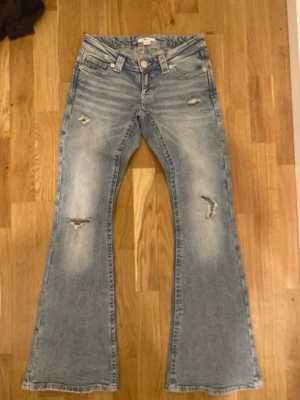 Ljusblå bootcut jeans med slitningar - Säljer ett par ljusblå bootcut jeans med slitningar och lätt tvättad look. Jeansen har fem fickor, låg midja och utställda ben. Snygga detaljer på bakfickorna och slitna partier framtill för en trendig vibe. Perfekta för dig som gillar retrostil. Säljer dessa byxor för de inte riktigt min stil och ångrar mitt köp. Om du har mer frågor om dessa byxor jätte gärna ställ några frågor så ska jag försöka mitt bästa att svara så noggrant som jag kan 💘💗