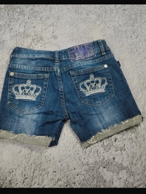 Victoria beckham jeans shorts storlek xs  - Säljer ett par blå jeansshorts från Betty Boop med slitna kanter och vita kronbroderier på bakfickorna. Shortsen har klassisk femficksdesign och en cool, avslappnad look. Perfekta för sommardagar och festivaler. Tror att dragkedjan är sönder men skulle nog kunna gå att laga vet faktiskt inte. Om man vill ha bild på det kan jag skicka privat och om mera frågor bara att skriva😊 har sytt igen lite längst ner vid kedjan eftersom den går av när den går ända ner. 