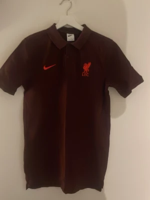Röd Liverpool pikétröja från Nike Storlek S och M - STycker du om Liverpool eller bara tycker att denna är snygg. Därför säljer jag denna helt oanvända limiterade vinröda pikétröja från Nike med Liverpool FC-logga och röd Nike-swoosh på bröstet. Storlek S men passar till M också. Skick 10/10. Tröjan har klassisk krage och korta ärmar, perfekt för dig som gillar fotboll och vill representera ditt lag med stil. Fråga om det är något du undrar över 😉