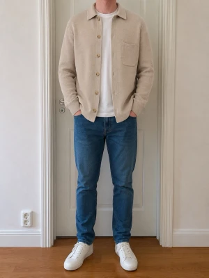 Beige stickad tröja  med knappar - Snygg beige stickad skjorta med klassisk krage och bröstficka. Skjortan har en rak passform, långa ärmar och stängs med knappar framtill. Perfekt att bära öppen över en t-shirt för en avslappnad look.