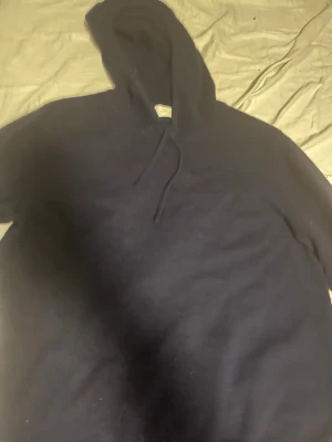 Mörkblå hoodie från Sayless  - Mörkblå hoodie från Sayless med klassisk huva. Tillverkad i mjukt material som känns skönt mot huden. Perfekt för dig som gillar en enkel och stilren look. Inga tryck eller mönster, bara clean och enkel design. De är 2 hål på ena armen man kan se de på sista bilden men inget man märker tydligt. Använt några gånger. Ny pris 1000kr 