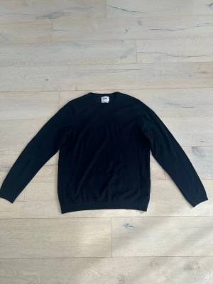 Mörkblå stickad tröja från NN07 - En stilren mörkblå tröja från NN07 med rund halsringning och långa ärmar. Tröjan har en klassisk passform och är tillverkad i ett mjukt, tunt material som passar perfekt till lager på lager. Enkel och tidlös design.