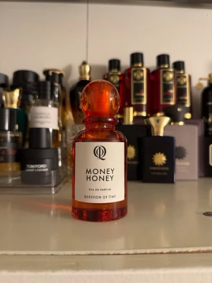 Money Honey Eau de Parfum - Money Honey Eau de Parfum från Question of Time kommer i en elegant, rund glasflaska i orange med matchande klotformad kork. Flaskan har en stilren etikett med svart text och sprayfunktion. Perfekt för dig som gillar unika och snygga parfymflaskor.