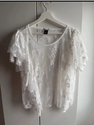 Vit spetsblus med volangärmar från lindex - Säljer en superfin vit blus i spets från lindex. Blusen har korta volangärmar och ett romantiskt blommigt spetsmönster. Den är lätt transparent och har rund halsringning. Perfekt att styla med jeans eller kjol för en trendig look.