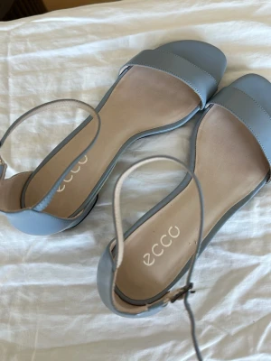 Ljusblå sandaler från ECCO - Snygga ljusblå sandaler från ECCO med öppen tå och justerbart ankelband. Tillverkade i slätt läder med mjuk innersula och svart gummisula för bra grepp. Minimalistisk design som passar perfekt till sommaren.