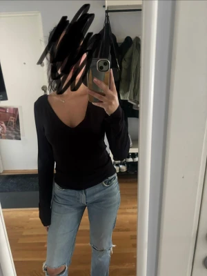Svart långärmad v-ringad topp - En svart långärmad topp med v-ringning och figurnära passform. Enkel och stilren design som passar till mycket. Perfekt att matcha med jeans eller kjol för en clean look.
