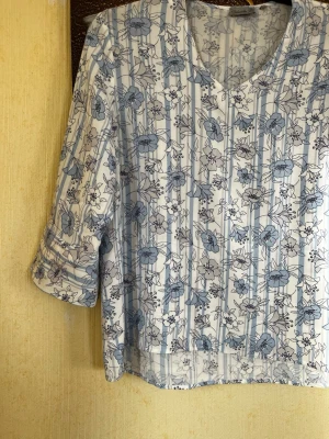 Blommig blus från Gabriella R - Ljusblå och vit blus med blommigt mönster och diskreta ränder. V-ringad hals och trekvartsärm. Tunt och lätt material, perfekt för en avslappnad och stilren look.