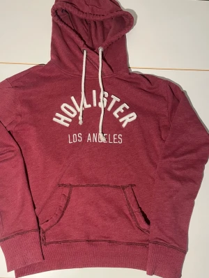 Vinröd hoodie från Hollister XS - Säljer en riktigt trendig vinröd hoodie från Hollister. Perfekt nu till sommaren. Skick 6/10 har ett hål vid fickan men inga andra defekter. Därav det billiga priset. 