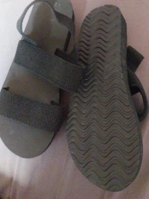Svarta sandaler med breda remmar - Snygga svarta sandaler med två breda textilremmar över foten och en hälrem. Sulan är platt och har vågigt mönster undertill för extra grepp. Perfekta för en avslappnad och trendig look.