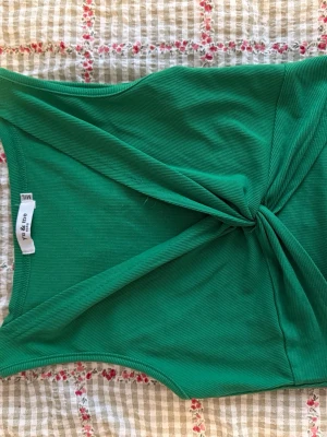 Grön ribbad tubtopp från Yu & Me - Snygg grön ribbad tubtopp från Yu & Me Paris. Toppen har en twistad detalj framtill som ger en cool look. Perfekt till sommaren och enkel att styla med både jeans och kjol. Materialet är mjukt och stretchigt för skön passform.