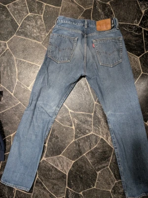 Levi's ljusblå raka jeans 28-30 - Klassiska ljusblå jeans från Levi's med rak passform och femficksdesign. Jeansen har en ikonisk läderpatch bak i midjan och röd Levi's-tagg på bakfickan. Tillverkade i slitstark denim, perfekta för en avslappnad och tidlös stil.