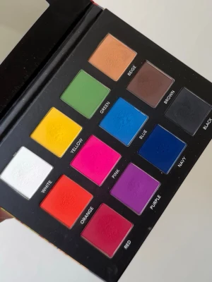 Färgstark ögonskuggspalett LH Cosmetics - Säljer en ögonskuggspalett från LH Cosmetics med tolv intensiva färger: vit, gul, orange, röd, rosa, lila, blå, marinblå, grön, beige, brun och svart. Paletten har fyrkantiga pans och ett färgglatt fodral med konstnärlig design. Använd fåtal gånger. 