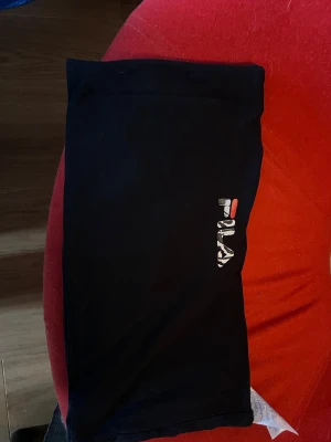 Svart bandeau topp från Fila - Svart bandeau topp från Fila med logga i vitt, rött och grönt framtill. Mjuk och stretchig, perfekt för chill dagar hemma eller som en del av din loungewear.