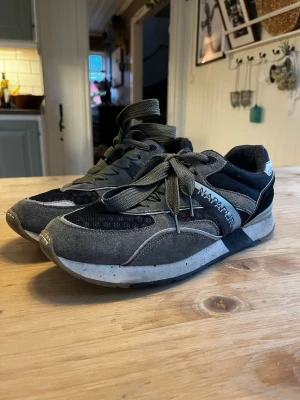 Napapijri grå och svarta sneakers - Snygga sneakers från Napapijri i grått och svart med coola detaljer. Ovandelen är i mocka och mesh, med gröna skosnören och en robust sula. Märkeslogga på sidan och bekväm passform, perfekt för en urban stil.
