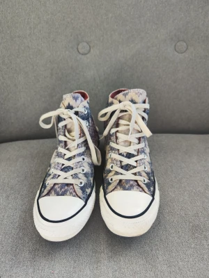 Converse x Missoni mönstrade sneakers - Unika Converse x Missoni high-top sneakers med ikoniskt zigzag-mönster i blått, vitt och beige. Klassisk vit gummisula och tå, vita skosnören och Missoni-tyg på ovandelen. Perfekta för dig som vill sticka ut med stilrena detaljer och cool design.