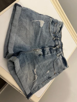 Blå denimshorts med slitningar - Snygga blå denimshorts med slitna detaljer och upprullade benslut. Super sköna och snygga!