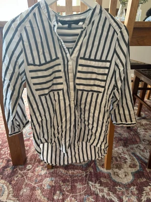 Randig vit och svart skjorta - Snygg skjorta från Vero Moda  i vitt med svarta ränder. Skjortan har trekvartsärm, två bröstfickor och knappar framtill. Perfekt för en trendig och avslappnad look.