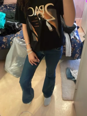 Svart Tupac t-shirt med tryck - Svart t-shirt med stort Tupac-tryck framtill och guldfärgat motiv på ryggen. Klassisk passform med korta ärmar och rund hals. Perfekt för dig som gillar streetstyle och vill ha en ikonisk look. Har använd den som pyjamas och passar jätte bra med ett par jeans shorts på sommaren