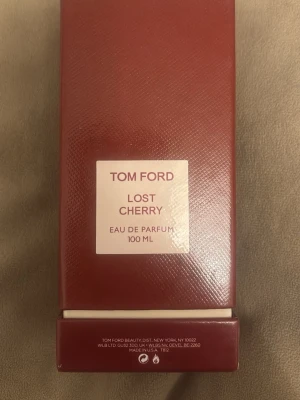Tom Ford Lost Cherry EdP 100 ml - Tom Ford Lost Cherry Eau de Parfum 100 ml kommer i en elegant mörkröd glasflaska med matchande kartong. Flaskan har en fyrkantig form och etikett i vitt med röd text. En lyxig doft som sticker ut med sin djupa körsbärsinspirerade design.