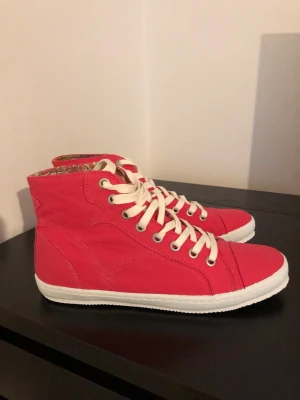 Röda high top sneakers med vita snören - Snygga röda high top sneakers med vita snören och vit sula. Skorna har en klassisk siluett och detaljerad sömnad. Insidan har ett mönstrat foder som ger en unik touch. Perfekta för dig som vill sticka ut med färg och stil.