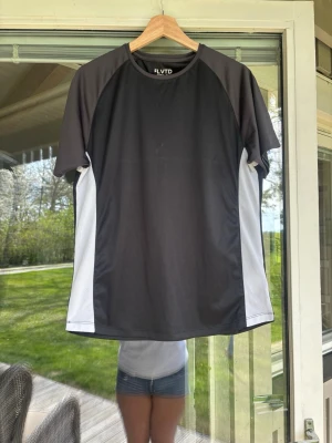 Svart och vit sporttröja från ELVTD - Sportig t-shirt från ELVTD i svart med vita paneler på sidorna och över ryggen. Tillverkad i ett lätt och ventilerande material, perfekt för träning eller löpning. Klassisk rund hals och korta ärmar ger en bekväm passform.