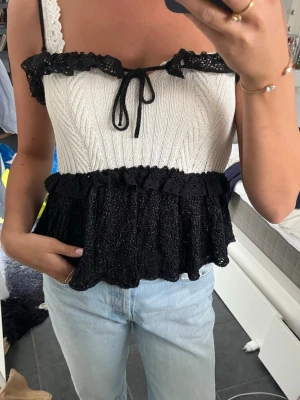 Vit och svart stickad linnetopp - Supersöt stickad topp i vitt och svart med volangdetaljer och knyt framtill. Perfekt att styla med jeans, kjol eller shorts nu till sommaren!🥰