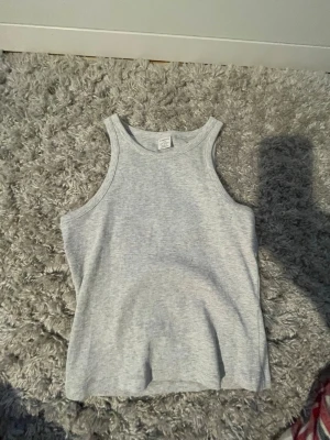 Ljusgrå ribbad linnetopp - Snygg ljusgrå ribbad linnetopp med klassisk rund halsringning och ärmlös design. Perfekt att styla till jeans eller shorts för en enkel och fräsch look. Mjuk och stretchig känsla.