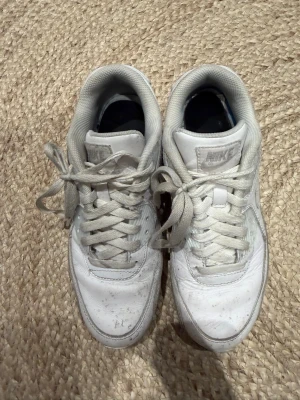Vita Nike Air Max90 - Säljer ett par klassiska vita Nike Air Max sneakers i läder med ikonisk sula och diskret Nike-logga på sidan. Skorna har lågt skaft och vita snören, perfekt för en clean och sportig look. Passar till det mesta och är riktigt bekväma att gå i.
