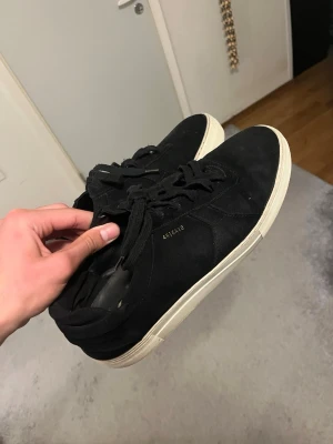 Svarta sneakers från Axel Arigato - Snygga svarta sneakers från Axel Arigato med ovandel i mocka och klassisk vit sula. Skorna har lågt skaft, svarta skosnören och diskret logga på sidan. Perfekta för en stilren och clean look.