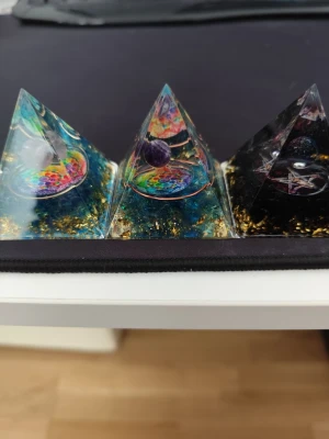 Färgglada orgonit pyramider med kristaller - Tre unika orgonit pyramider i transparent resin med färgglada detaljer, koppartråd, guldflingor och infällda kristaller. Varje pyramid har en rund mandala och en kristallkula inuti, perfekt som dekoration eller för energi.