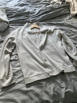 Beige cardigan med knappar - Säljer en stilren beige cardigan med knäppning framtill och långa ärmar. Tröjan har en mjuk, strukturerad yta och en avslappnad passform. Perfekt att slänga över en t-shirt för en chill look.