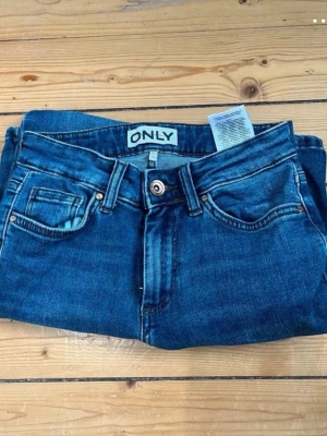 Blå bootcut jeans från ONLY - Snygga blå bootcut jeans från ONLY med klassisk femficksdesign och normalhög midja. Jeansen har en lätt utsvängd passform nertill och är tillverkade i denim med stretch för extra komfort. Perfekta för en trendig och avslappnad look. Storleken är XS 30