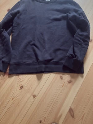 Svart crewneck från cp company - En svart sweatshirt med rund hals och långa ärmar. Tröjan har en klassisk, enkel design utan tryck eller mönster och är tillverkad i mjukt material. Perfekt för en avslappnad stil.