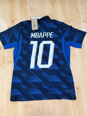 Mbappé #10 – Player Edition Frankrike (storlek M) - Mbappé #10-tryck. Player Edition Frankrike. Storlek M. Helt ny och aldrig använd. Säljs i befintligt skick. Skickas snabbt! 🚚💨  Mått för denna tröja (storlek M): (Uppmätta av leverantör – viss variation kan förekomma) • Halva bröstmåttet: 51 cm • Tröjans längd: 72,5 cm • Ärmbredd: 22,5 cm • Axelbredd: 43 cm • Ärmlängd: 39 cm • Manschettbredd: 18 cm  🔥 Player Edition-modell – tajtare passform än vanliga supportertröjor. 🇫🇷 Frankrike landslag.