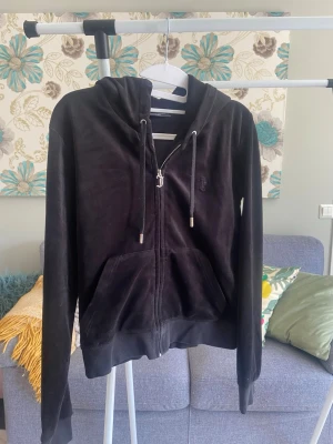 Svart Juicy Couture hoodie med dragkedja - Svart hoodie i mjuk velour från Juicy Couture med dragkedja framtill, huva med snören och två stora fickor. Klassisk logga broderad på bröstet. Den är i mycket fint skick men tröjan är använd fåtals gånger.