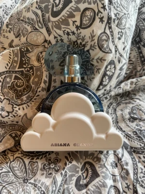 Ariana Grande Cloud Parfym - Superfin parfym från Ariana Grande i en unik blå glasflaska med molnformad vit bas och blått moln som lock. Flaskan är både söt och stilren, perfekt att ha framme på hyllan. Doften är populär och flaskan känns lyxig och modern.Är använd några få gånger, säljer då jag har en annan oarfym som jag använder mer. 