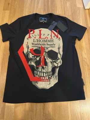 Philipp Plein svart t-shirt med dödskalle - Svart t-shirt från Philipp Plein med stor glittrig dödskalle framtill, röda och vita tryckdetaljer. Helt ny, XXL men passar Xl