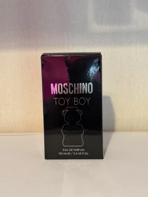 Moschino Toy Boy Eau de Parfum 100ml - Moschino Toy Boy Eau de Parfum i en unik svart flaska formad som en nallebjörn. Flaskan rymmer 100 ml och har en modern, lekfull design med silvriga detaljer och Moschino-loggan framtill. Perfekt för dig som gillar trendiga och iögonfallande parfymer.
