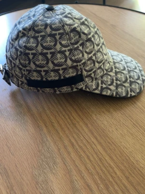 Beige keps med mönster från Salvatore Ferragamo - Hej, jag säljer denna feregamo kepsen den har används i max en vecka sen så märkte jag att den satt konstigt och problemet var att mitt huvud var för stort. Så om fu har några frågor är det bara att slå en pling☺️ ingen kartong men ni kan få lapp om de behövs.