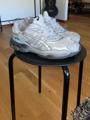 Asics silvriga sneakers med mesh - Säljer ett par silvriga Asics sneakers med klassisk mesh och syntetpaneler. Skorna har grå och vita detaljer samt en svart och grå sula. Asics-loggan syns på sidan och tungan. Perfekta för dig som gillar sportig och retro stil.