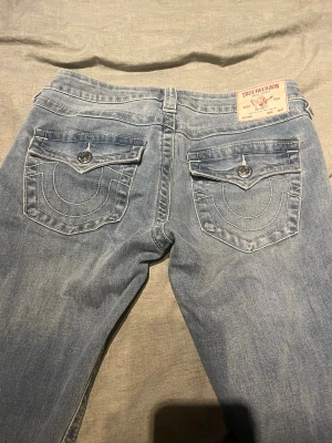 True Religion ljusblå bootcut jeans - Ljusblå jeans från True Religion med bootcut-modell och klassiska kontrastsömmar. Snygga fickdetaljer med lock och knappar bak samt ikonisk logga på bakfickan. Tillverkade i denim med en cool, avslappnad vibe.