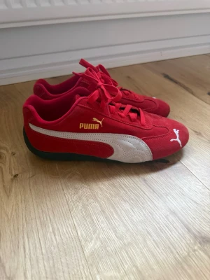  Puma Speedcat Sneakers storlek 39 - Snygga röda sneakers från Puma med klassisk vit formstripe på sidan och guldfärgad logga. Ovandelen är i mocka och skon har svarta sulor. Perfekta för dig som vill sticka ut med en sportig och retro stil.