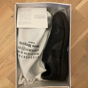 Svarta  Maison Margiela gats  - Säljer ett par schysta gats från Maison Margiela i storlek 41. Dem är lite små i storleken och innersulamått är 25cm. Dem är i nyskick, ända grejen är att lådan samt dustbagen har lite skador men annars är dem i nyskick! 