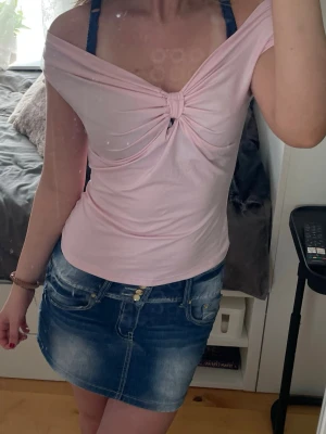 Ljusrosa off shoulder topp - Söt ljusrosa topp med off shoulder-design och knutdetalj framtill. Toppen är ärmlös och har en mjuk, stretchig passform som sitter snyggt över axlarna. Materialet känns lätt och bekvämt mot huden.