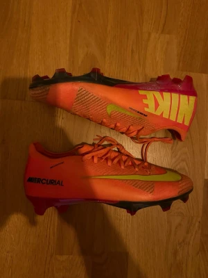 Nike Mercurial - Säljer ett par Nike Mercurial cosmic speed fotbollsskor i en riktigt schysst orange färg med limegröna detaljer och svart sula. Skorna har låg profil, snörning och är tillverkade i syntetmaterial för bästa känsla och grepp på planen. Perfekta för dig som vill sticka ut på matchen!