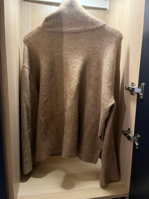 Beige stickad polotröja - Mysig beige stickad polotröja med bred ribbstickad kant nedtill och vid ärmsluten. Tröjan har en avslappnad passform och hög polokrage, perfekt för kyliga dagar. Mycket fint och bra material.
